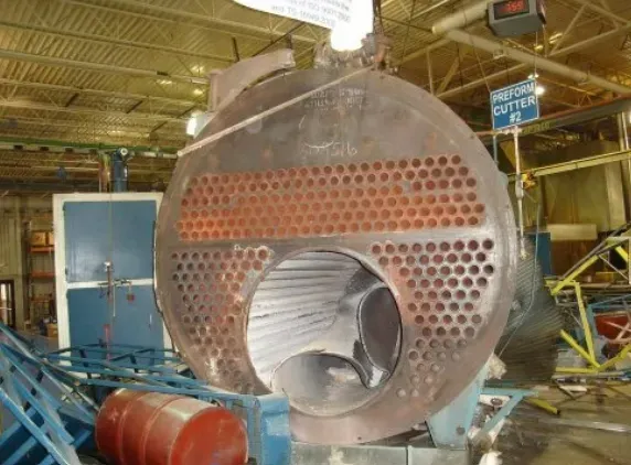Large, open industrial boiler with numerous holes, showing interior tubes in a factory setting.