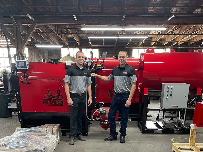 Two men are standing next to each other in a warehouse in front of a red machine.